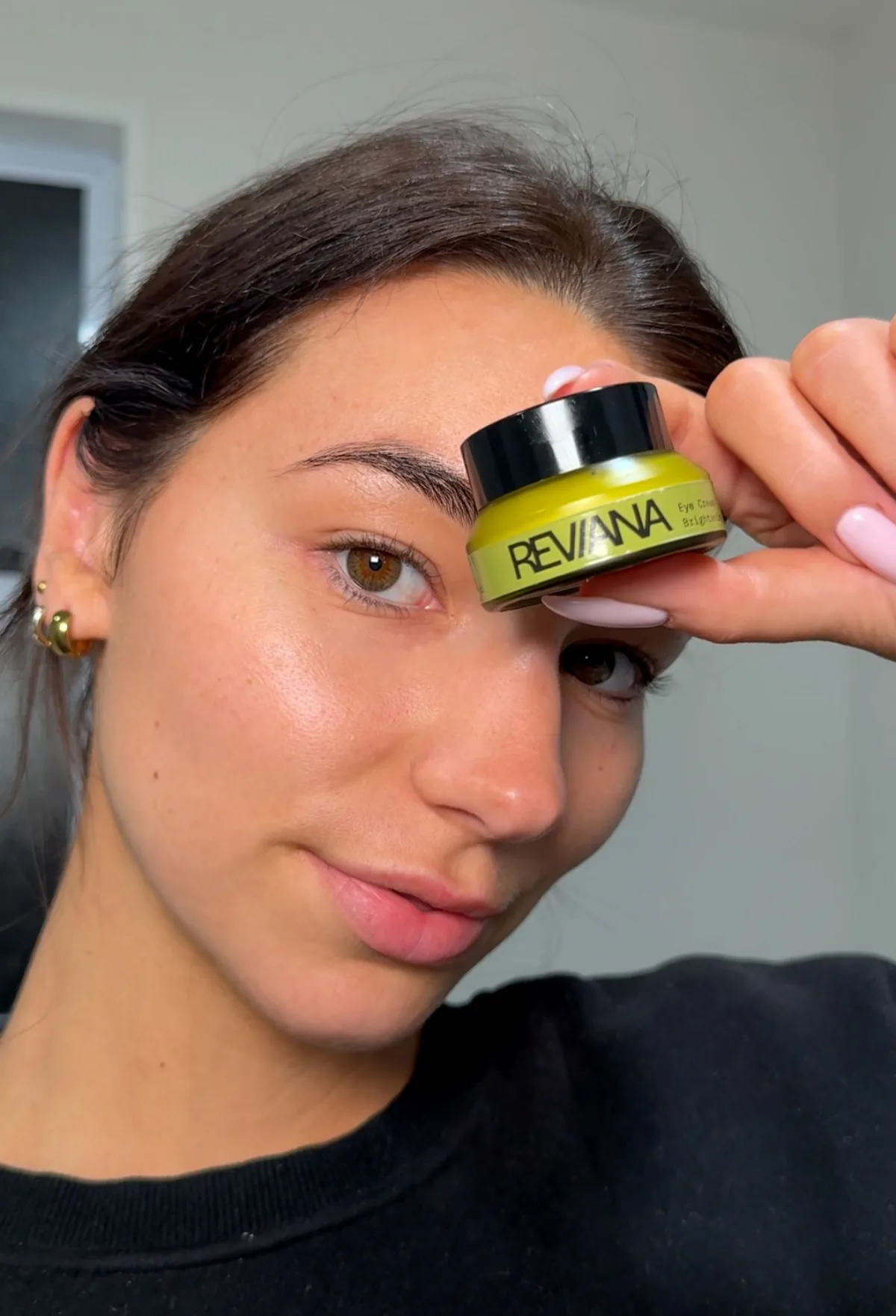 Woman holding the real Eye Cream jar beside her eye